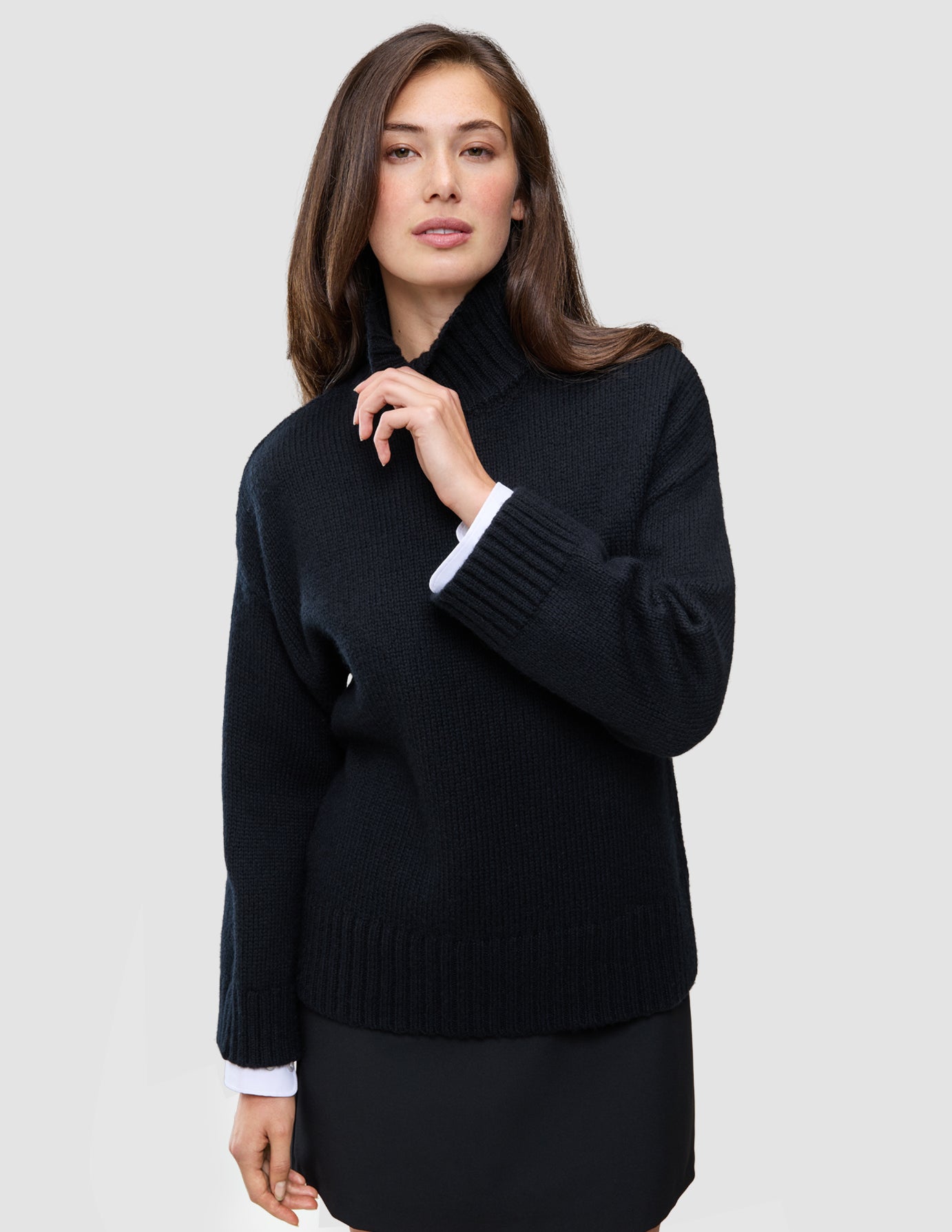 Kvinne iført en svart, tykk og myk ullstrikket turtleneck for kvinner, med hvite skjorte mansjetter som stikker frem.